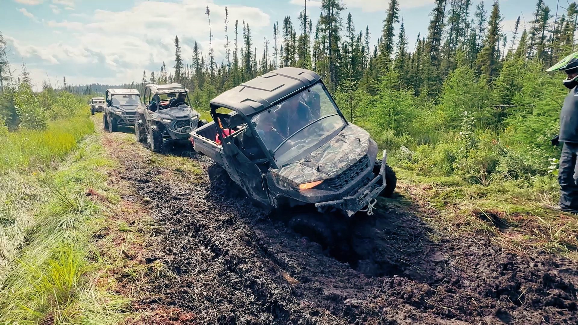 A side-by-side pushes through deep mud with the convoy waiting behind