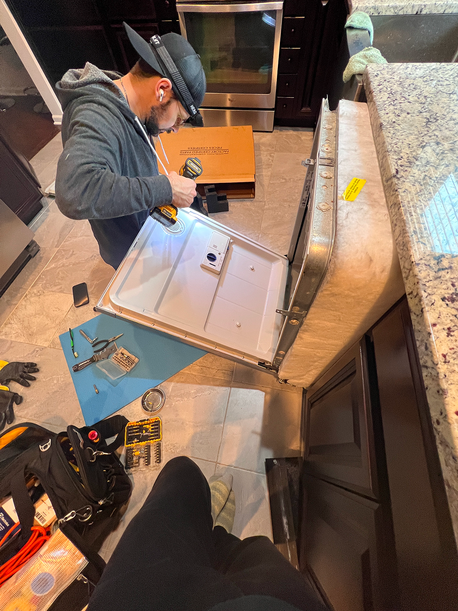 Appliance repair technician working on a dishwasher door and control panel.