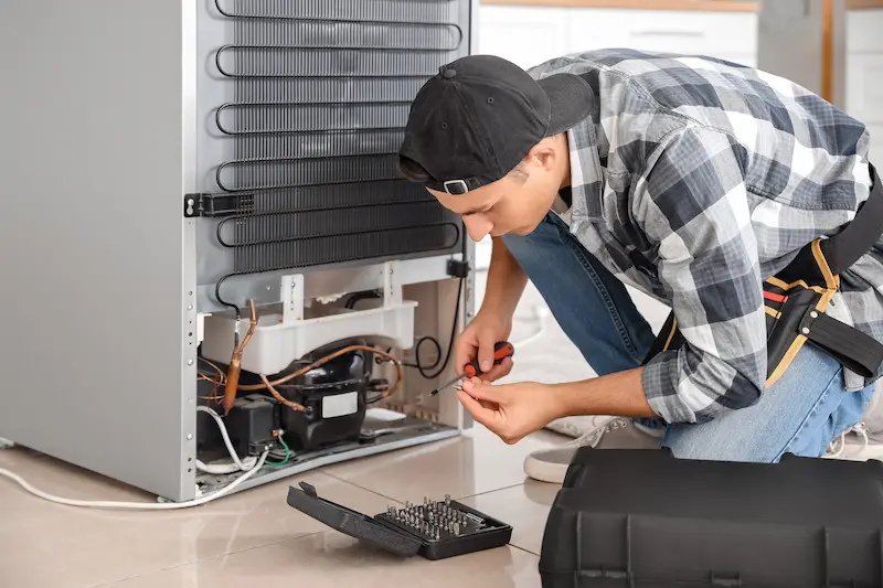 Technician repairing refrigerator compressor with screwdriver during appliance service