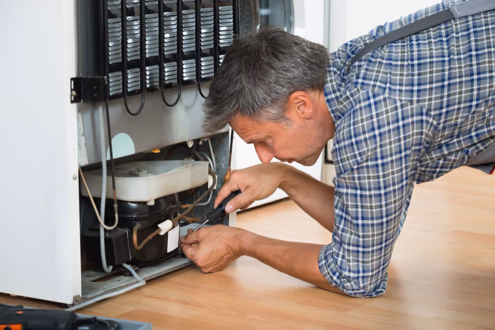 Technician repairing refrigerator compressor at the back of fridge — cooling issue repair