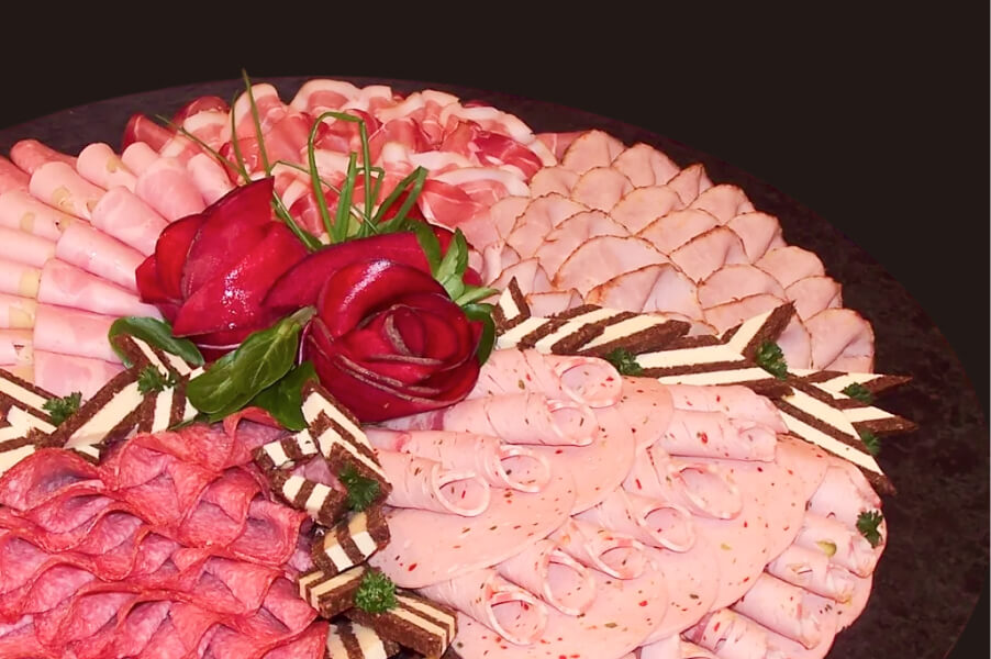 Platte mit kunstvoll arrangierten, verschiedenen Wurst- und Schinkensorten, dekoriert mit frischen Kräutern.