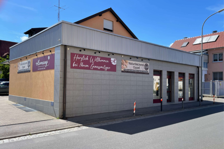 Die Filiale Knetzgau, die Sonne scheint von oben, Reklametafeln mit Logo von Genussmetzgerei Horung und Bäckerei Oppel