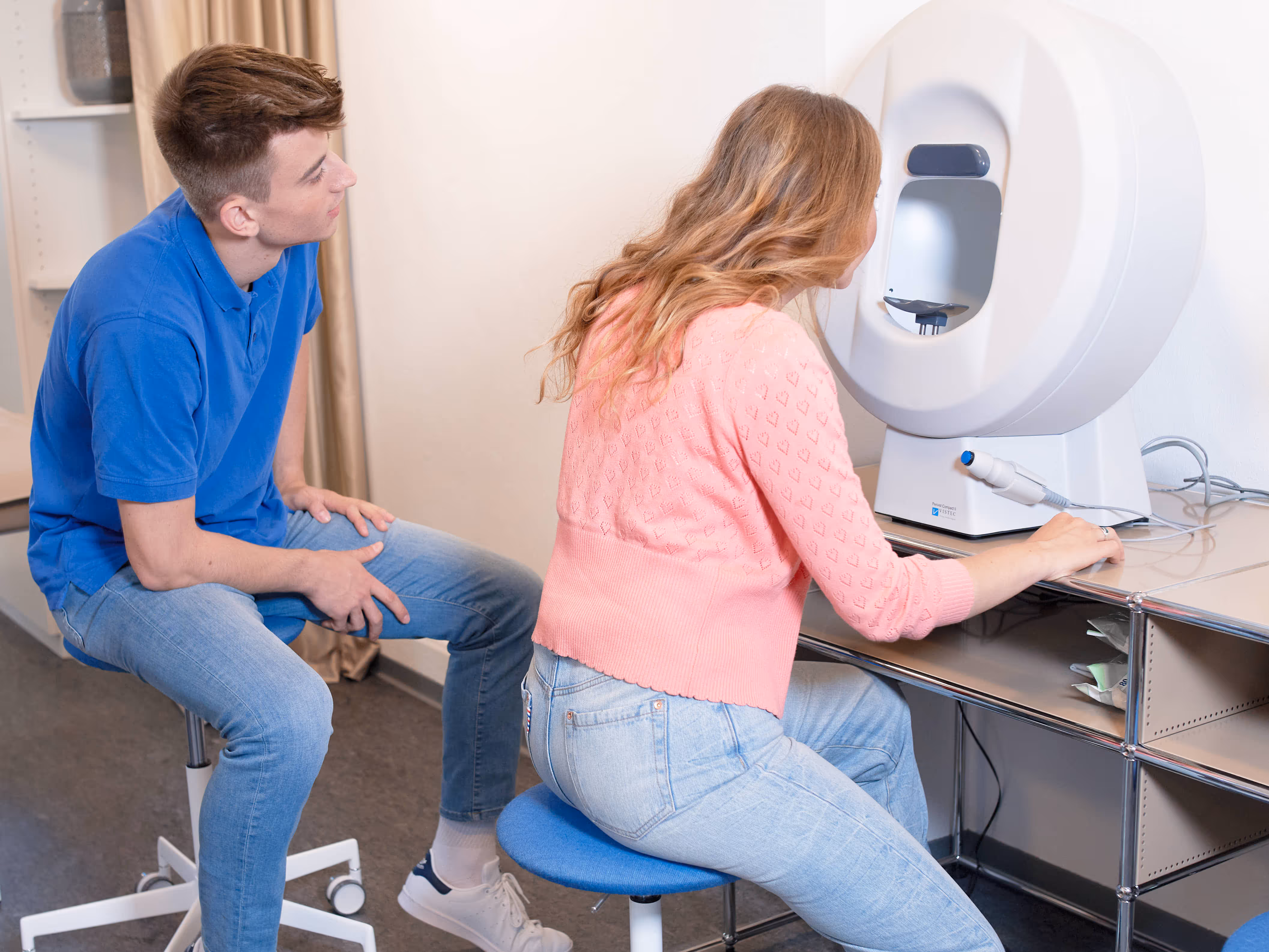Junge Optikerin untersucht Patientenauge: Moderne Sehtest mit Autorefraktor in stilvoller Praxis.