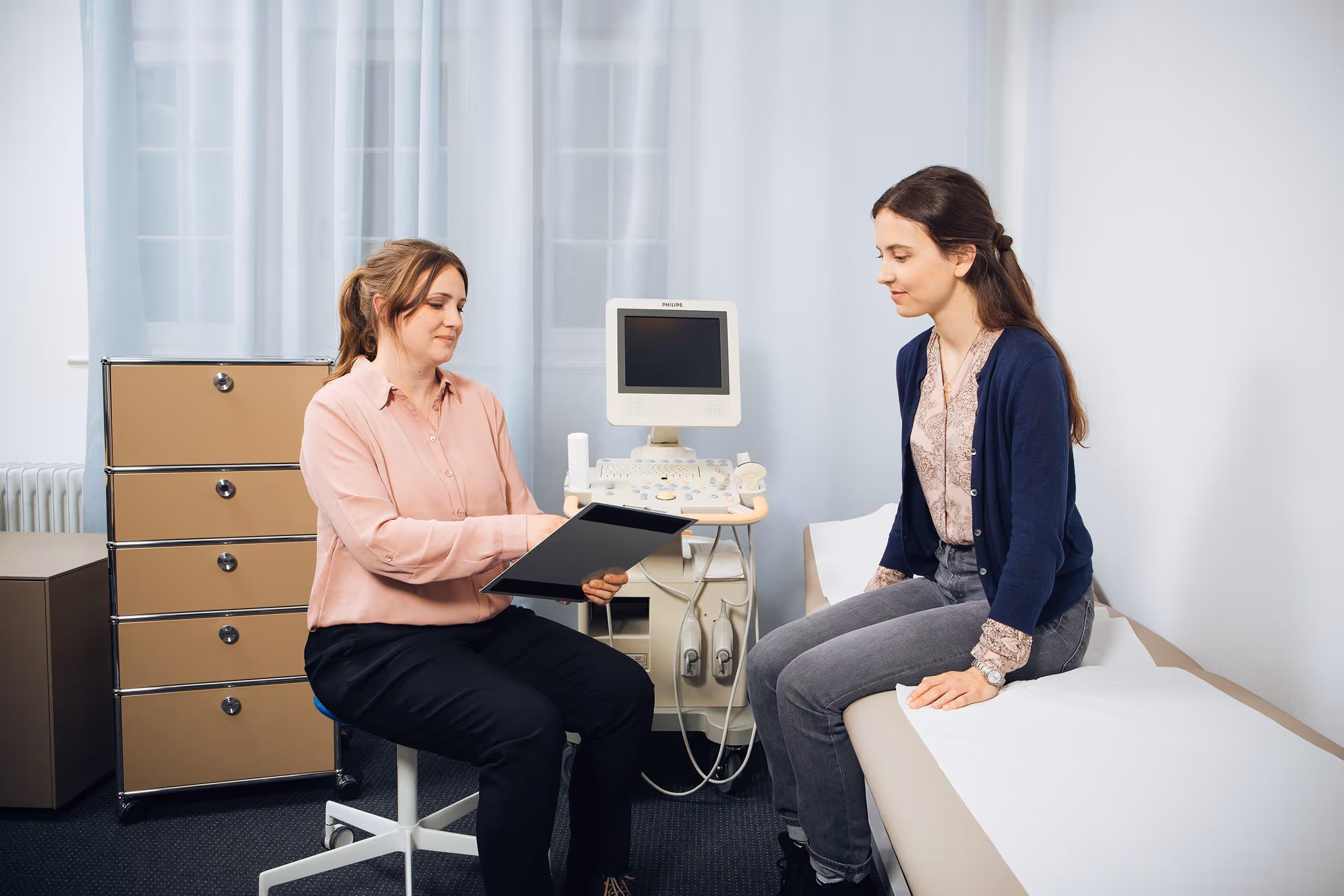 Ärztin berät Patientin in moderner Praxis: Ultraschalluntersuchung mit Philips-Gerät, professionelle Gesundheitsberatung.