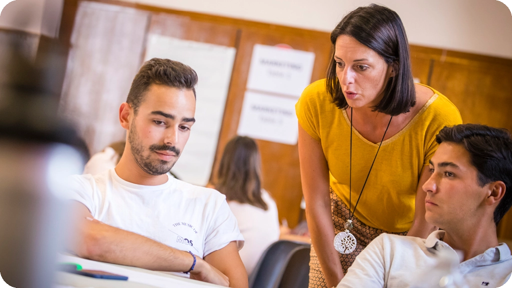 Enseignante accompagnant deux étudiants lors d’un travail en classe, dans une ambiance studieuse et collaborative.
