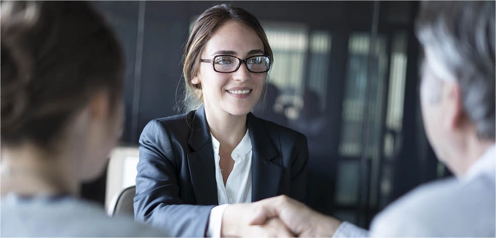 Jeune femme en costume lors d’un entretien professionnel serrant la main d’un recruteur.