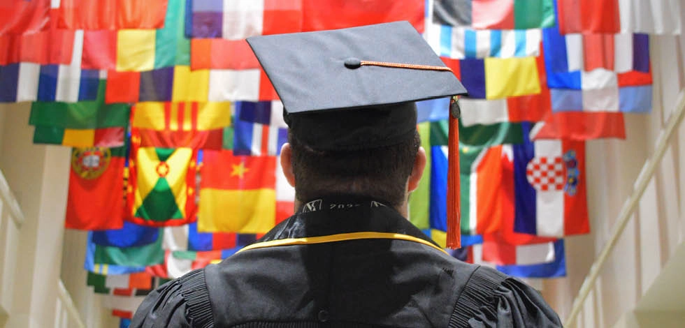 Étudiant diplômé en toge universitaire faisant face à une mosaïque de drapeaux internationaux, symbolisant une carrière mondiale - BSB