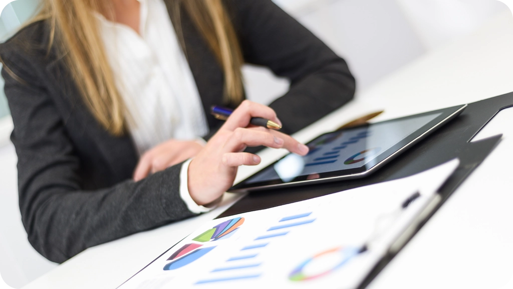 Femme en costume analysant des graphiques financiers sur une tablette avec des documents de suivi budgétaire sur la table, illustrant les missions du contrôleur de gestion – BSB
