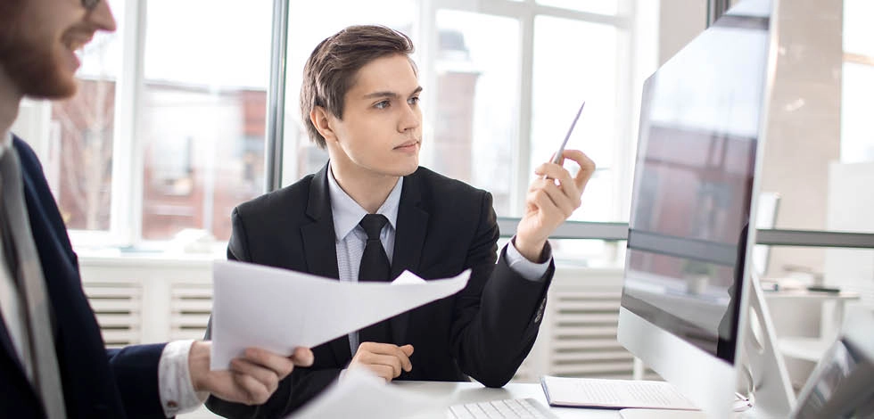 Jeune professionnel en costume analysant des documents financiers devant un ordinateur, illustrant le rôle d’analyse et de pilotage budgétaire du contrôleur de gestion – BSB