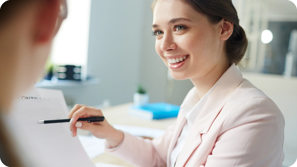Une jeune conseillère bancaire souriante en veste rose échange avec un client dans un bureau lumineux, illustrant les débouchés professionnels après un BTS Banque. - BSB