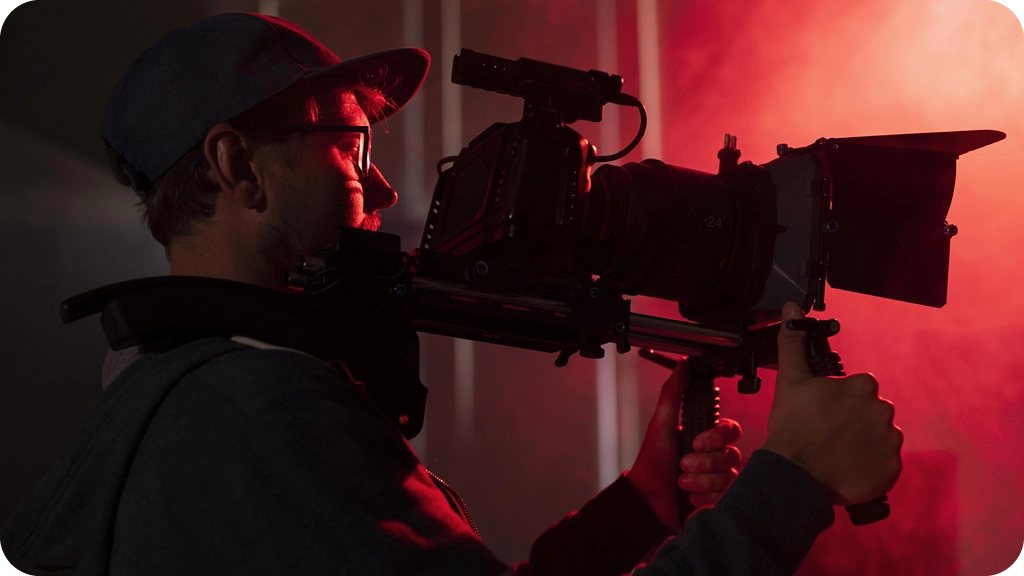 Un cadreur en pleine action filme avec une caméra professionnelle épaulée, éclairé par une lumière rouge en studio – BSB.