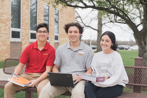 Carmel Catholic students sitting together with laptops outside