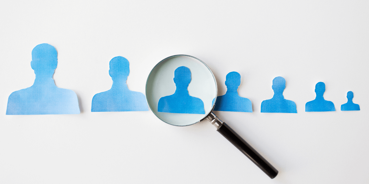 A magnifying glass highlights one blue paper silhouette in a row.