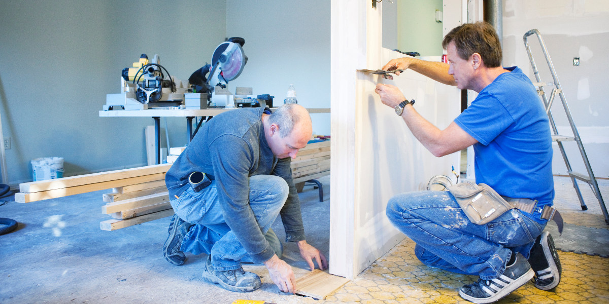 Two contractors working together on a door frame inside a home under renovation