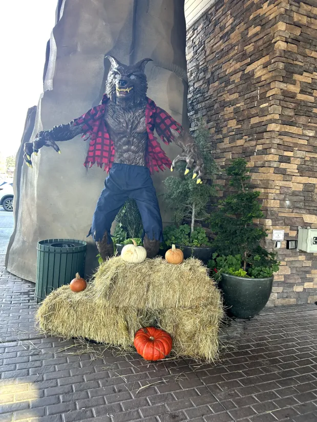 A Halloween-themed decoration featuring a scarecrow surrounded by hay bales, pumpkins, and potted plants, displayed at the Great Wolf Lodge.