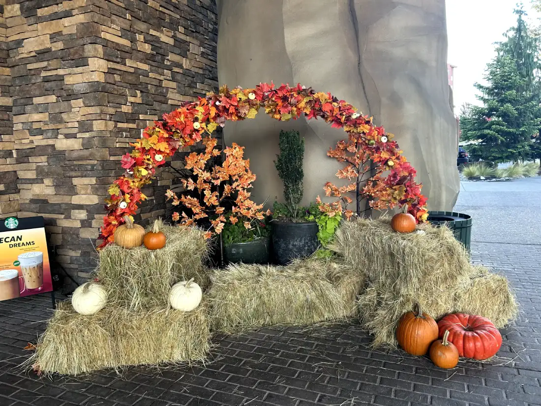 A festive autumn arrangement with hay bales, pumpkins, and colorful fall foliage under a decorative arch at the entrance of the Great Wolf Lodge.