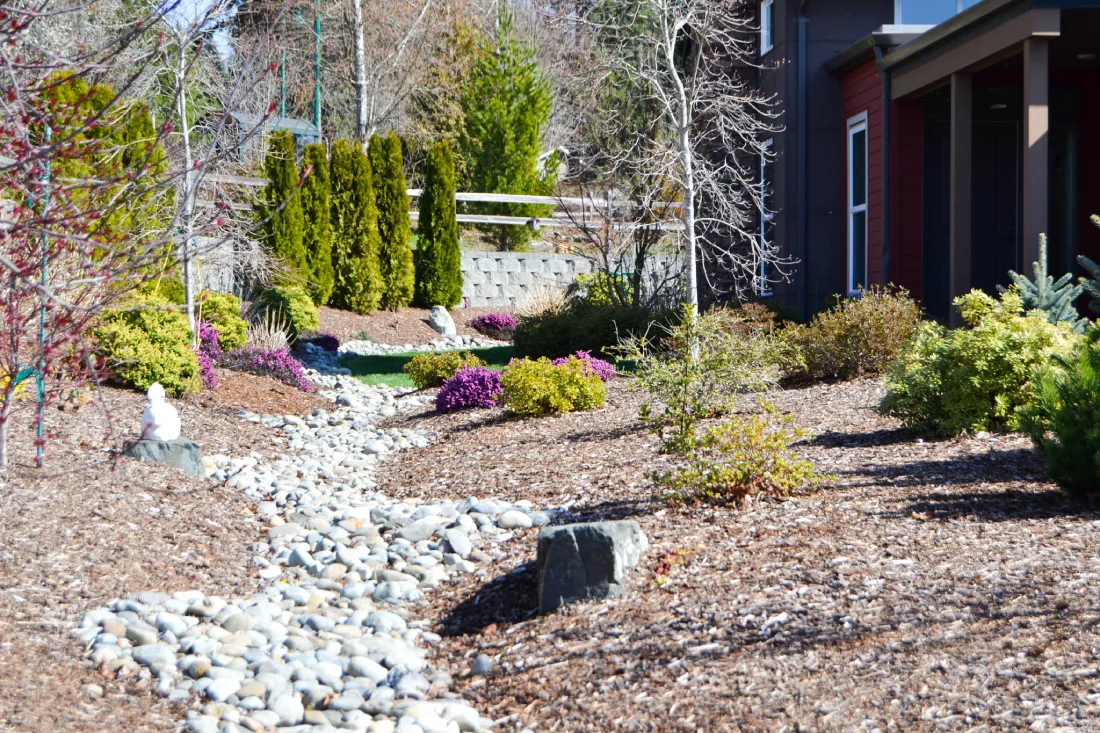 A beautifully landscaped area at Heron's Key featuring a decorative dry creek bed, mulched flower beds, and vibrant greenery, reflecting professional care and design.