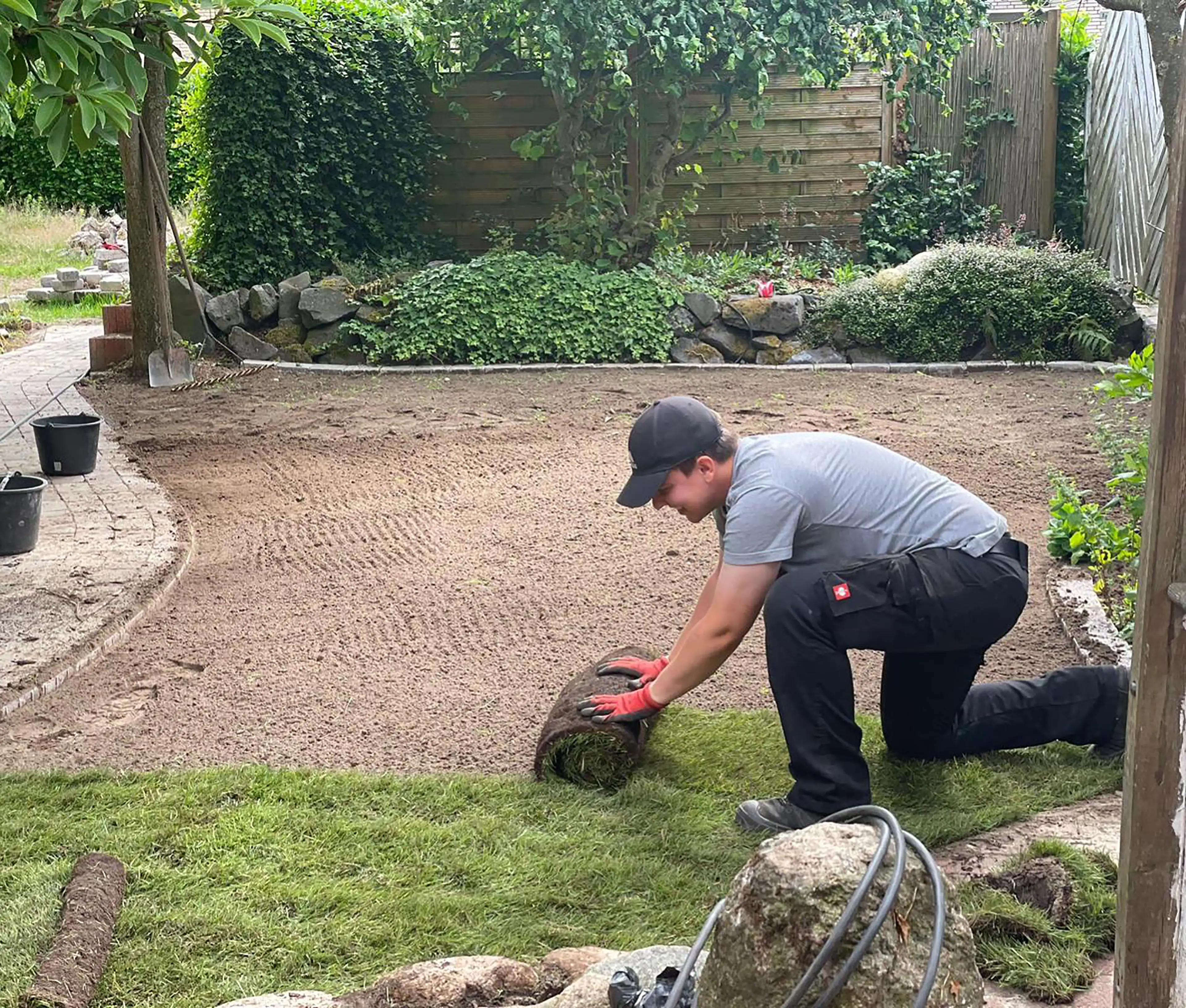 Mann kniet und verlegt Grasnarbe auf einem vorbereiteten Boden in einem Garten.