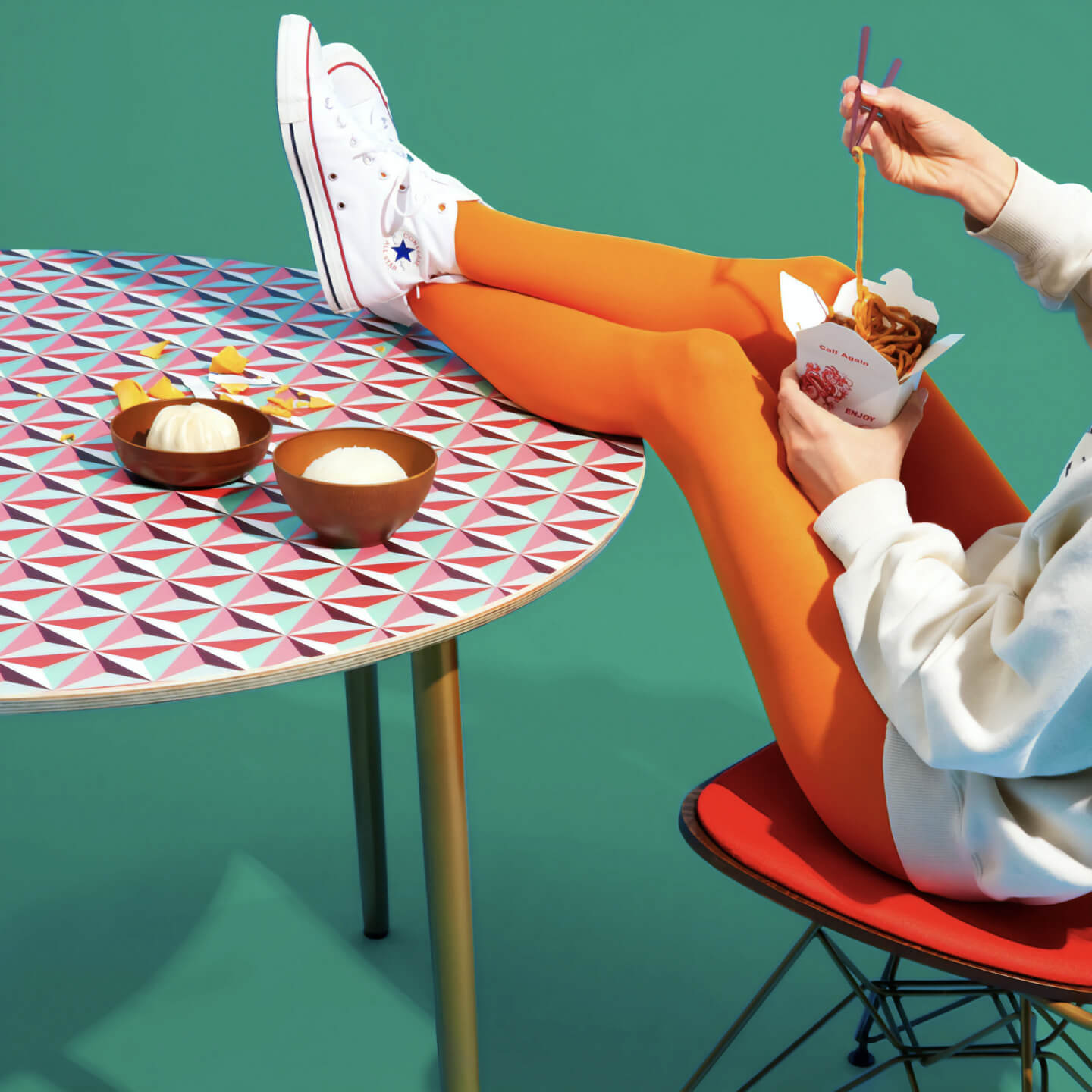Green background with table and person with legs on table, eating takeout.