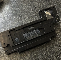 A metal component sample by KT Machining. The component has many notes and paths carved into it, likely to slide onto other components.