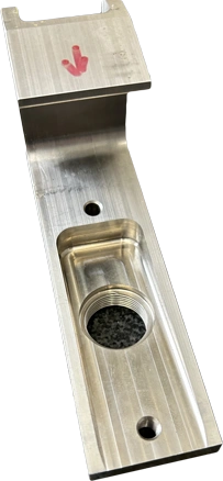 A metal component sample from KT Machining. It looks like a bracket meant to fit one specific way onto other components, forming a hook shape with various holes and spaces carved into its side.