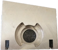 A KT Machining sample component which has two small rectangle holes on each side of a large hole, with notches carved in the face of the component to the sides of the hole.