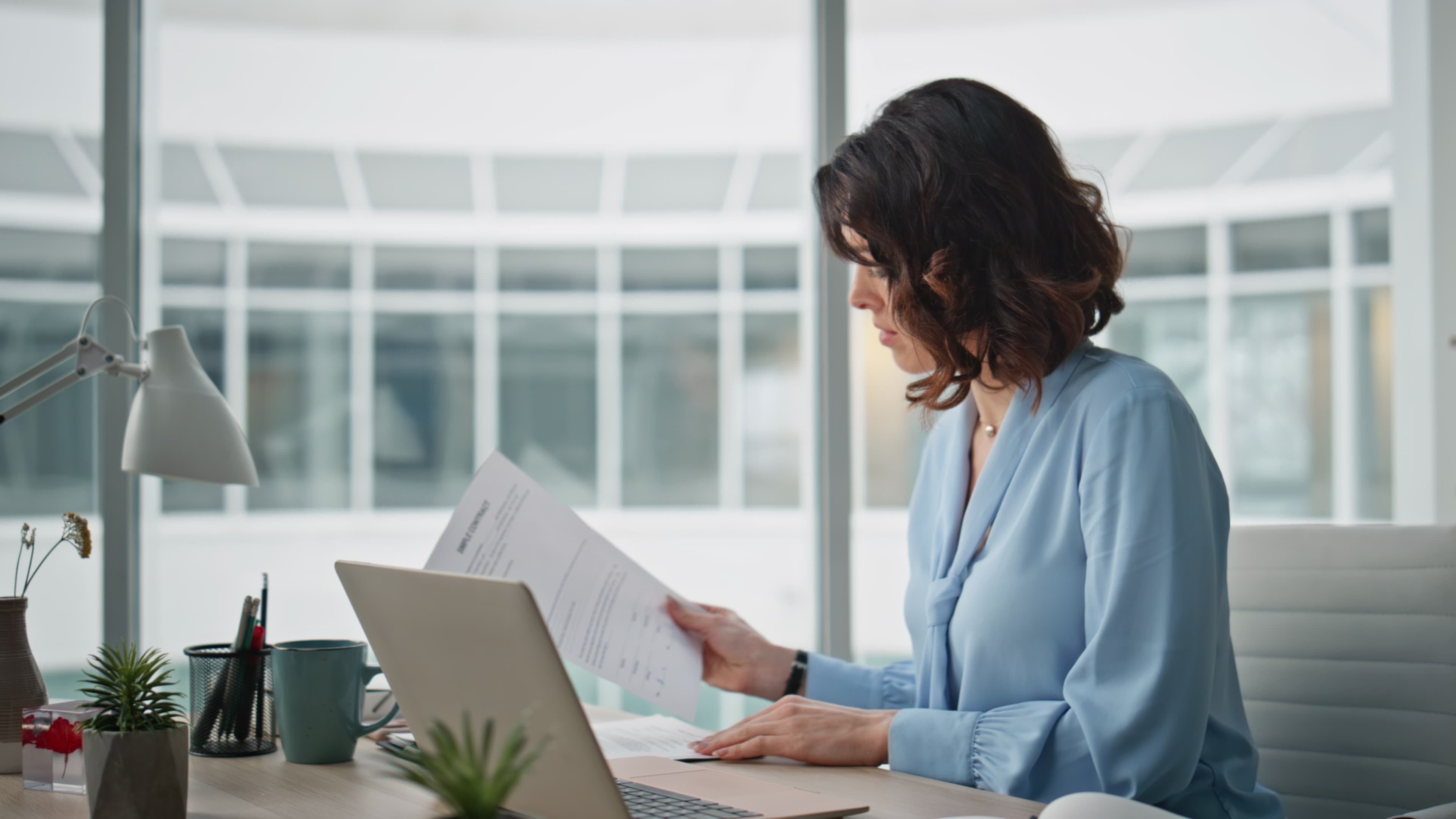 Focused accountant working laptop at desk office handling documents closeup.