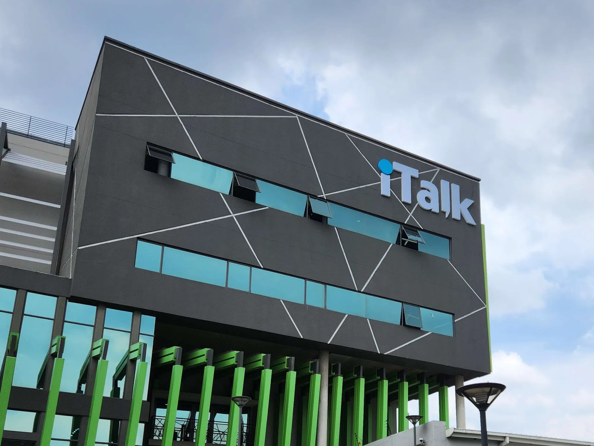 Modern building facade with blue windows, green vertical beams, and iTalk logo on top corner.