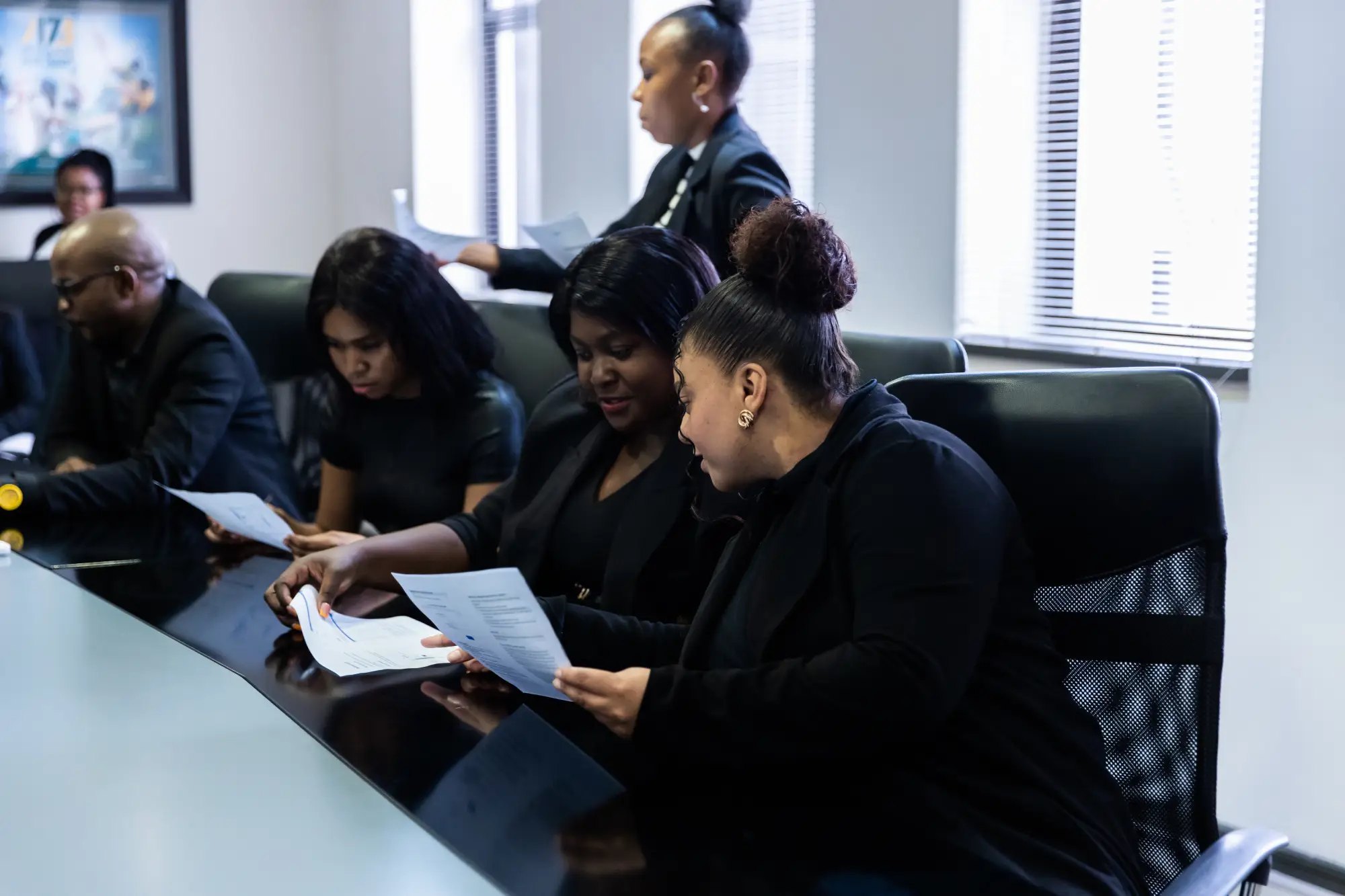 Group of people in black clothes sitting at a conference table reviewing documents.