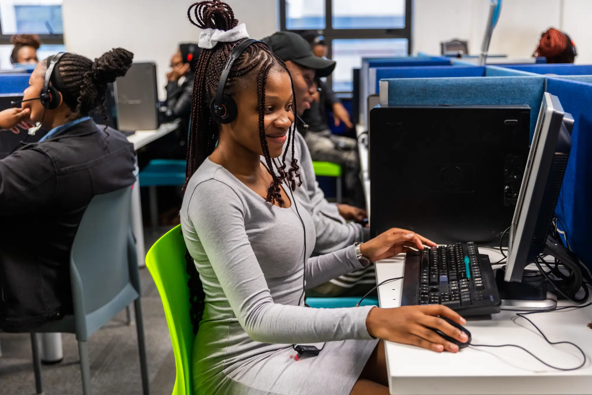 Young woman with headset working on a desktop computer in a busy call center.