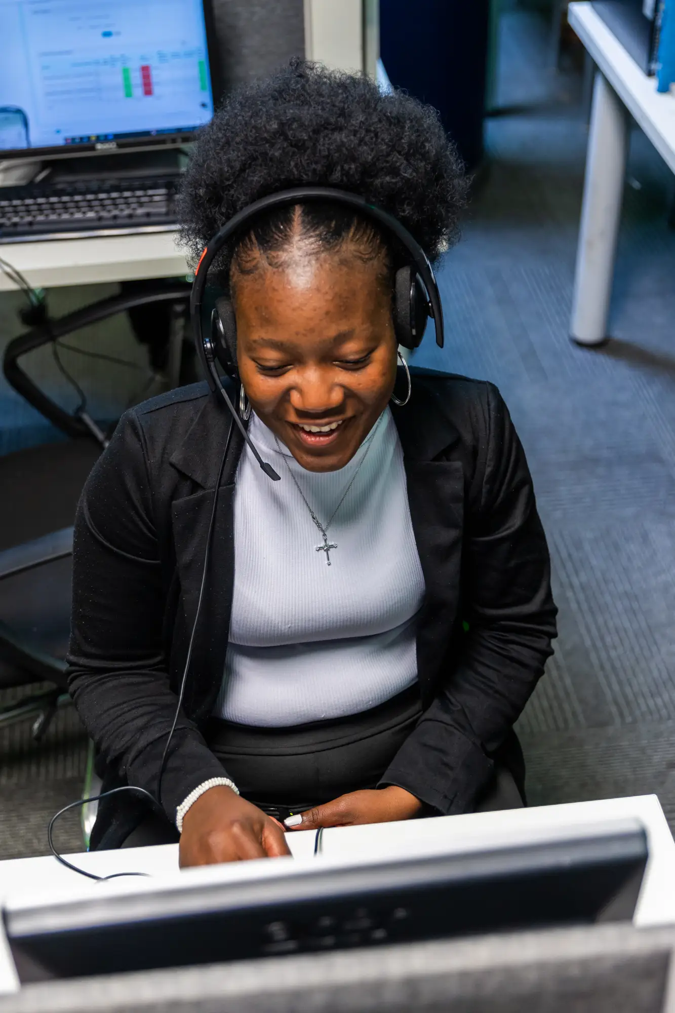 Smiling woman with headset working at a computer desk in an office setting.