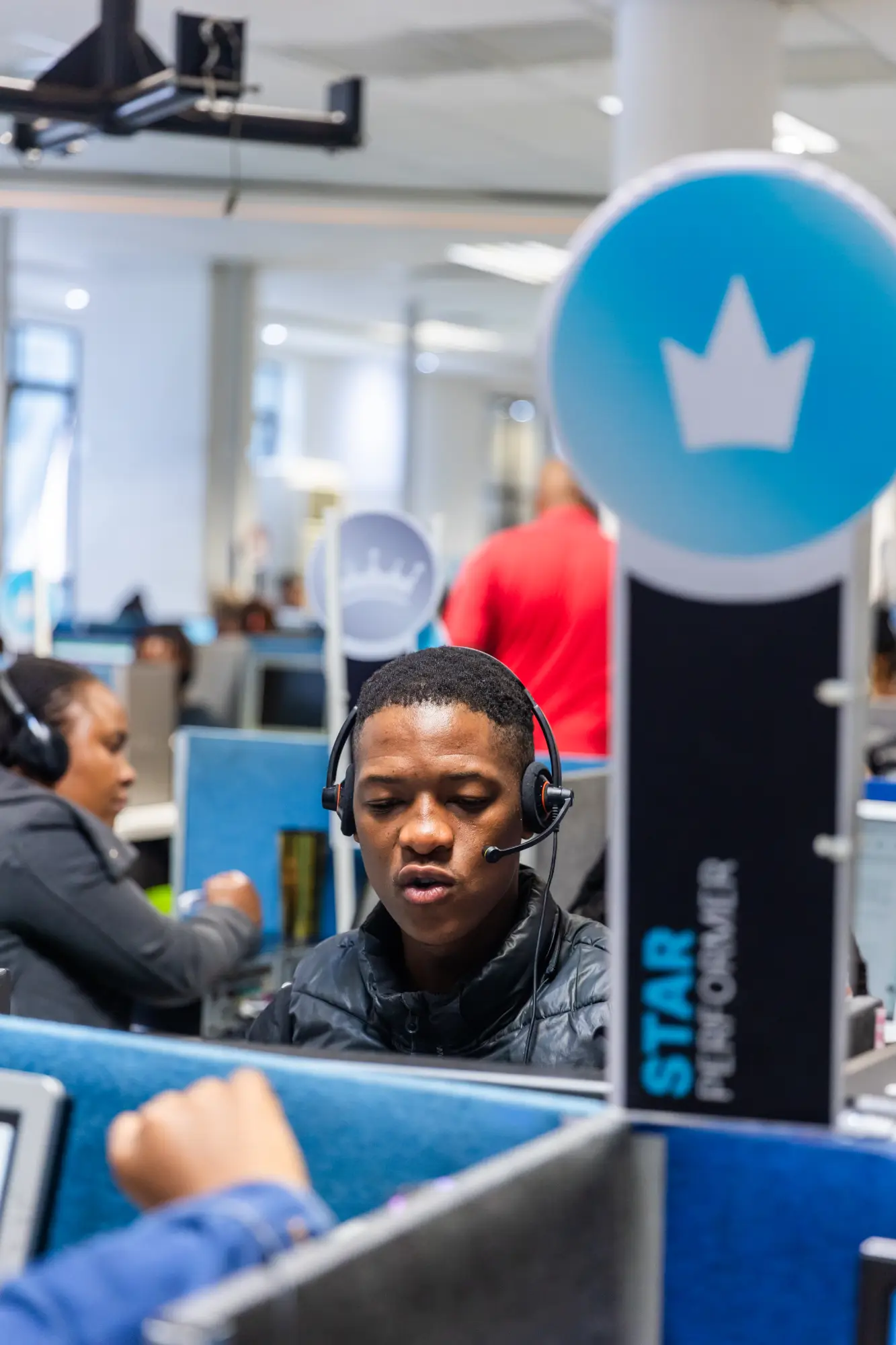 Man wearing headset working in a busy office with blue cubicles and a Star Performer sign.