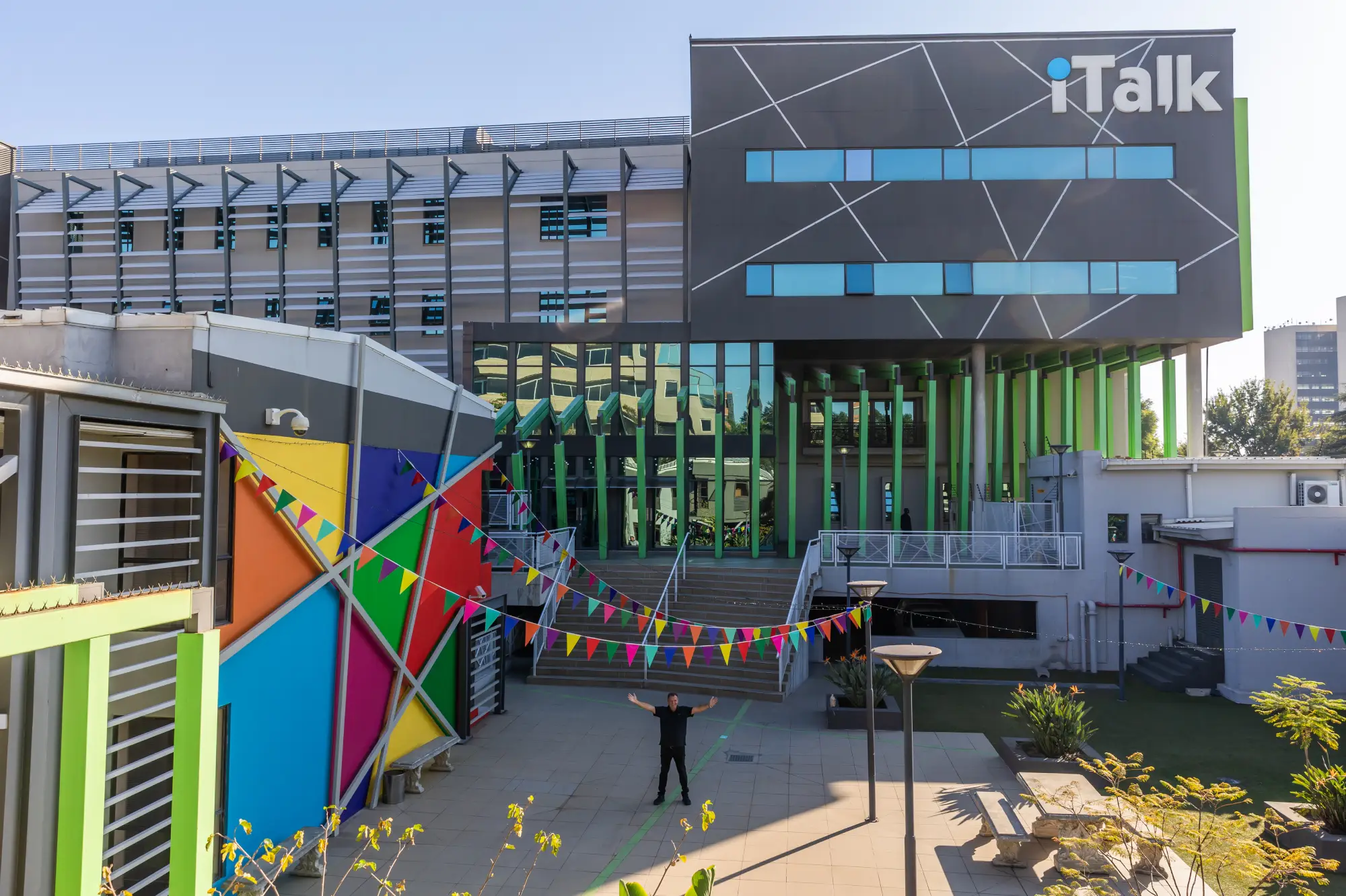 Person standing with arms raised in front of modern building with colorful panels and iTalk logo.
