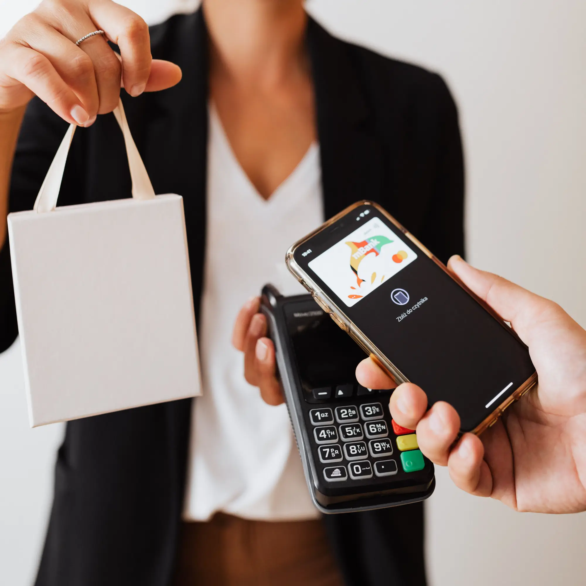 Person holding a white shopping bag and card reader, another uses phone for contactless payment.
