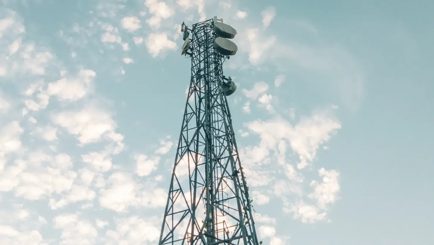 Telecommunication tower with antennas against a blue sky with scattered clouds.