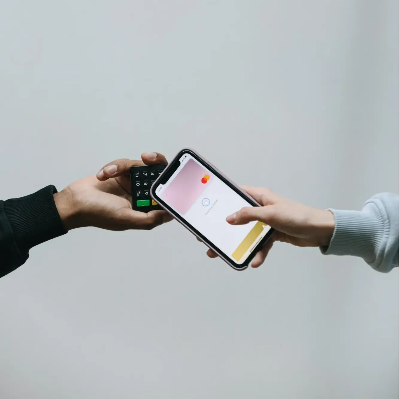 Person holding smartphone with digital Mastercard near card reader held by another person.