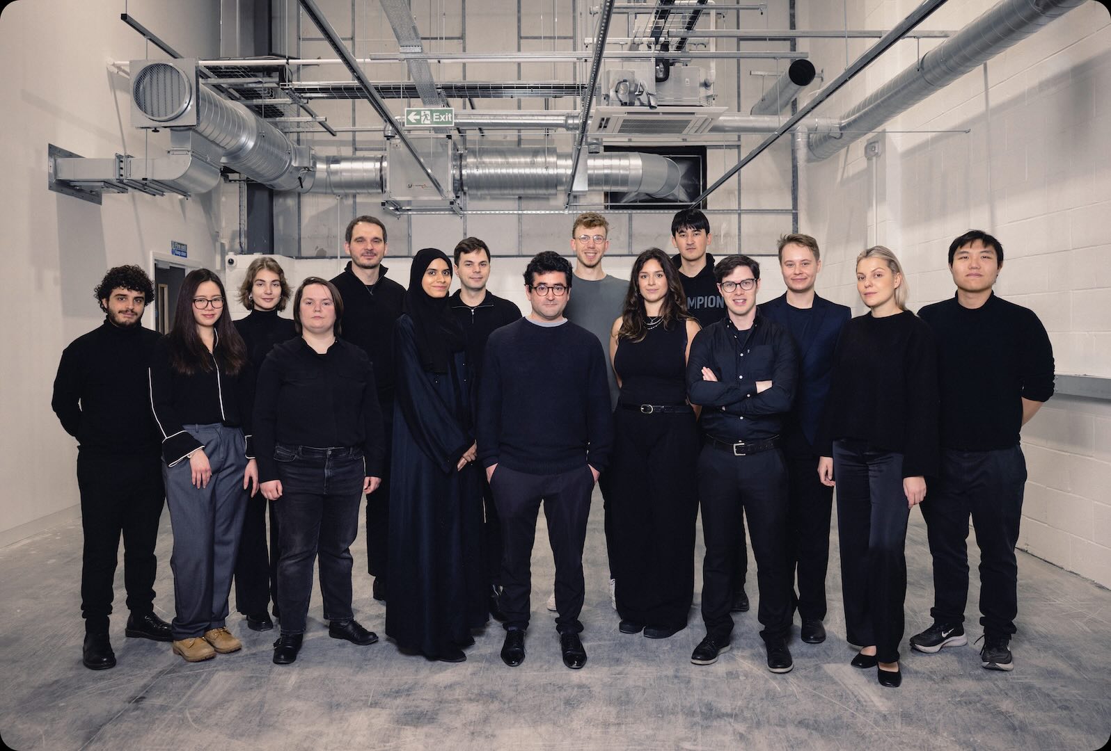 Diverse group of fifteen young professionals standing in an industrial-style room.