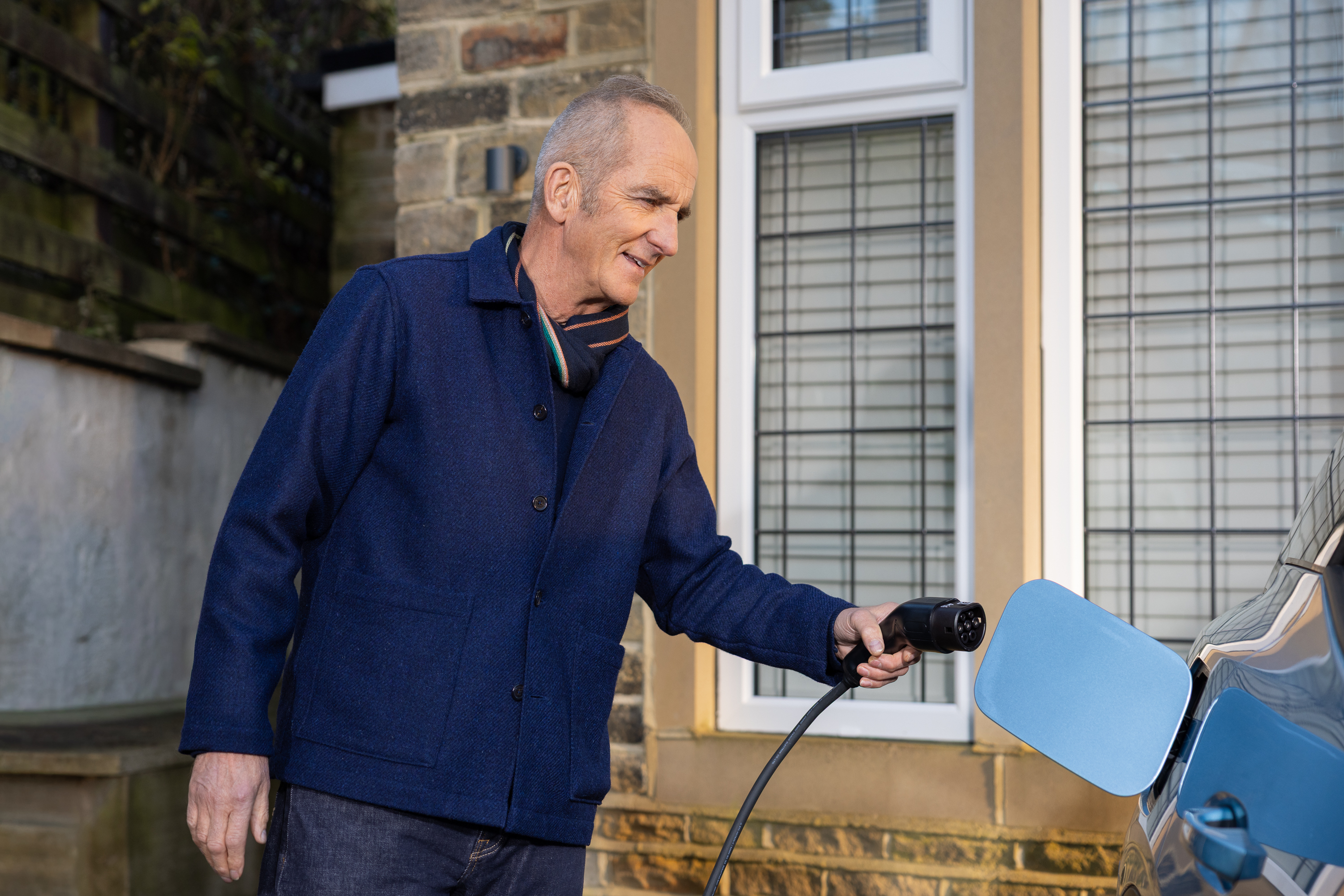 Kevin McCloud plugging an EV charger into a car.
