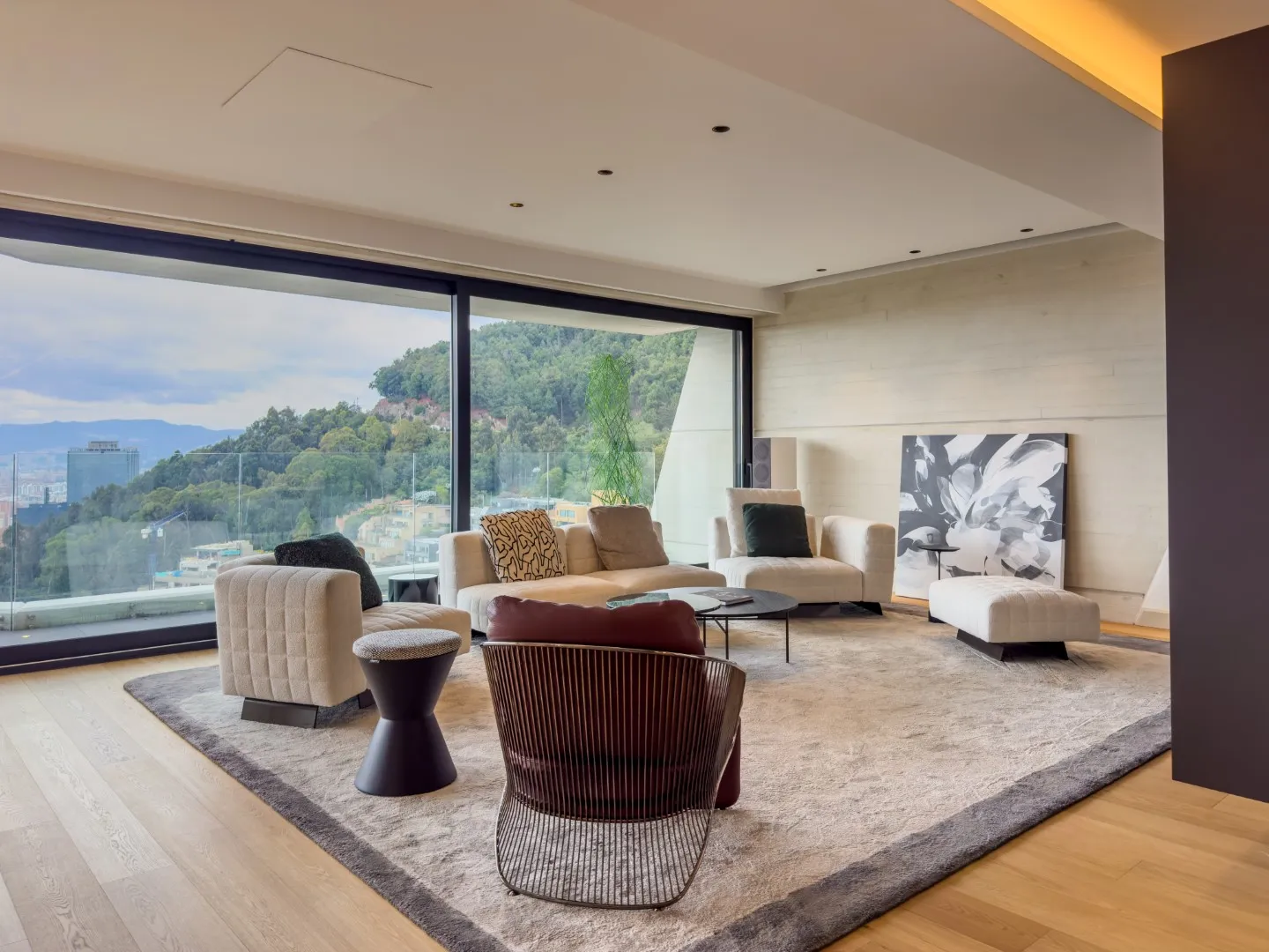 Sala moderna con sofá, sillas, mesa negra y ventanal con vista a colina verde.