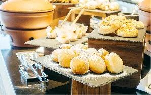 Pães variados frescos empilhados em tábuas de madeira em um buffet.
