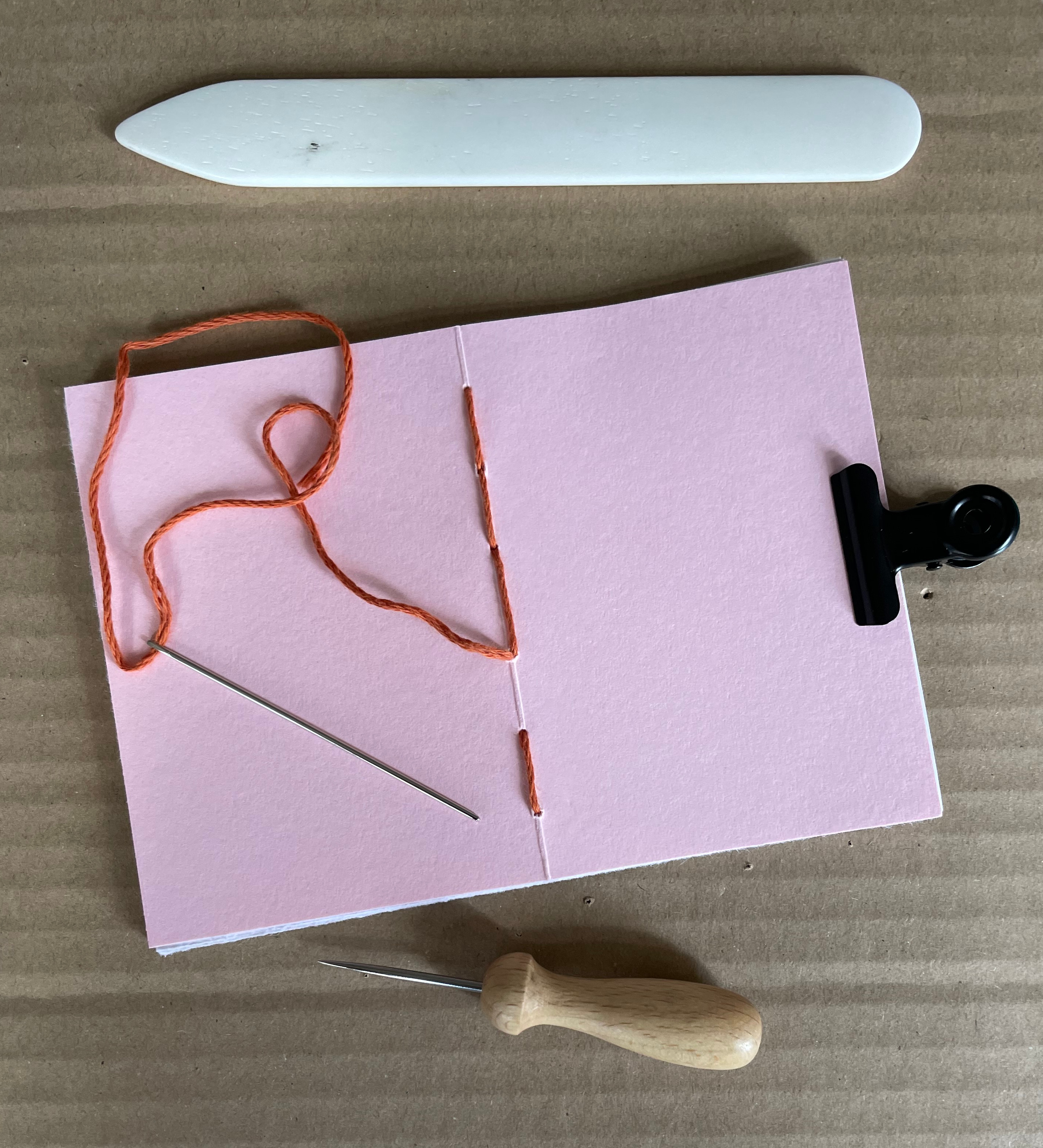 Utensilien zum Heftbinden und ein halbfertig gestaltetes Heft in rosa.