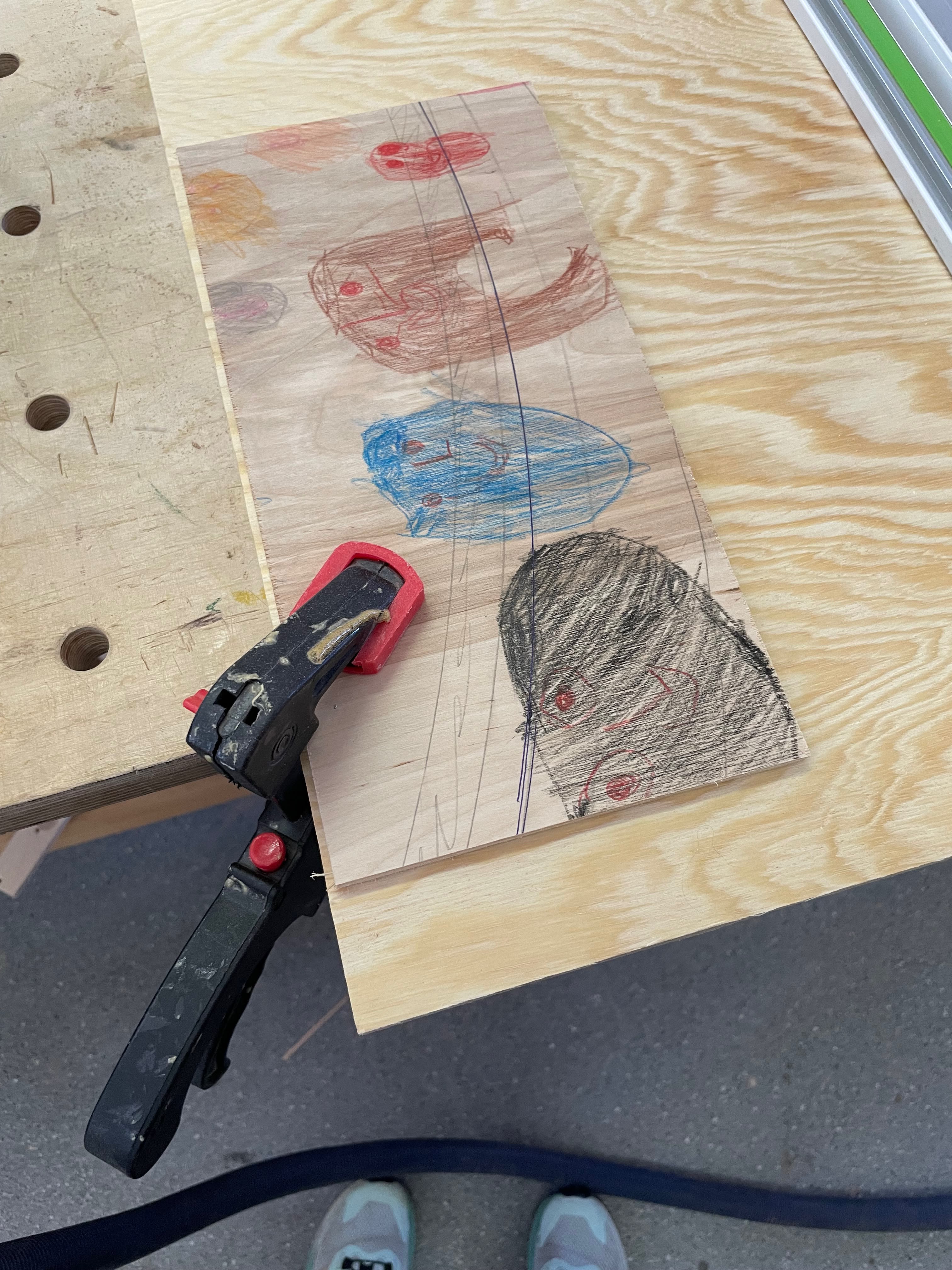 Foto aus einer Holzwerkstatt. Ein bemaltes Stück Holz festgeklemmt auf einem Werktisch.