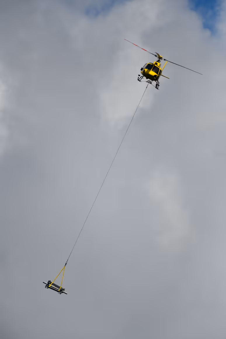yellow helicopter using a long line to transport heavy machinery parts