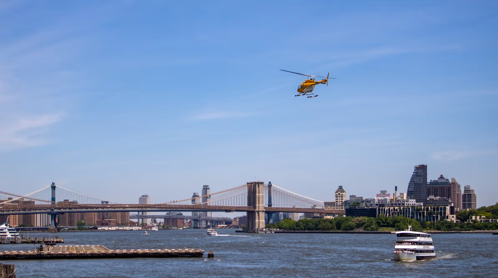 white and yellow helicopter flying toward the Brooklyn Bridge in New York