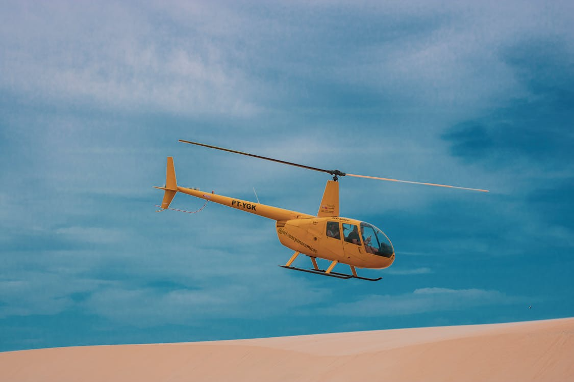 yellow helicopter flying over a sand dune under blue skies