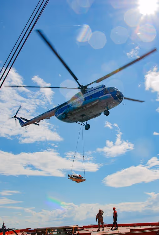 blue and white heavy-lift helicopter lifting cargo on ropes above a platform