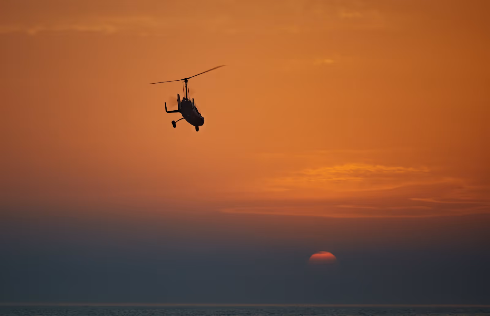 silhouette of a helicopter flying at sunset