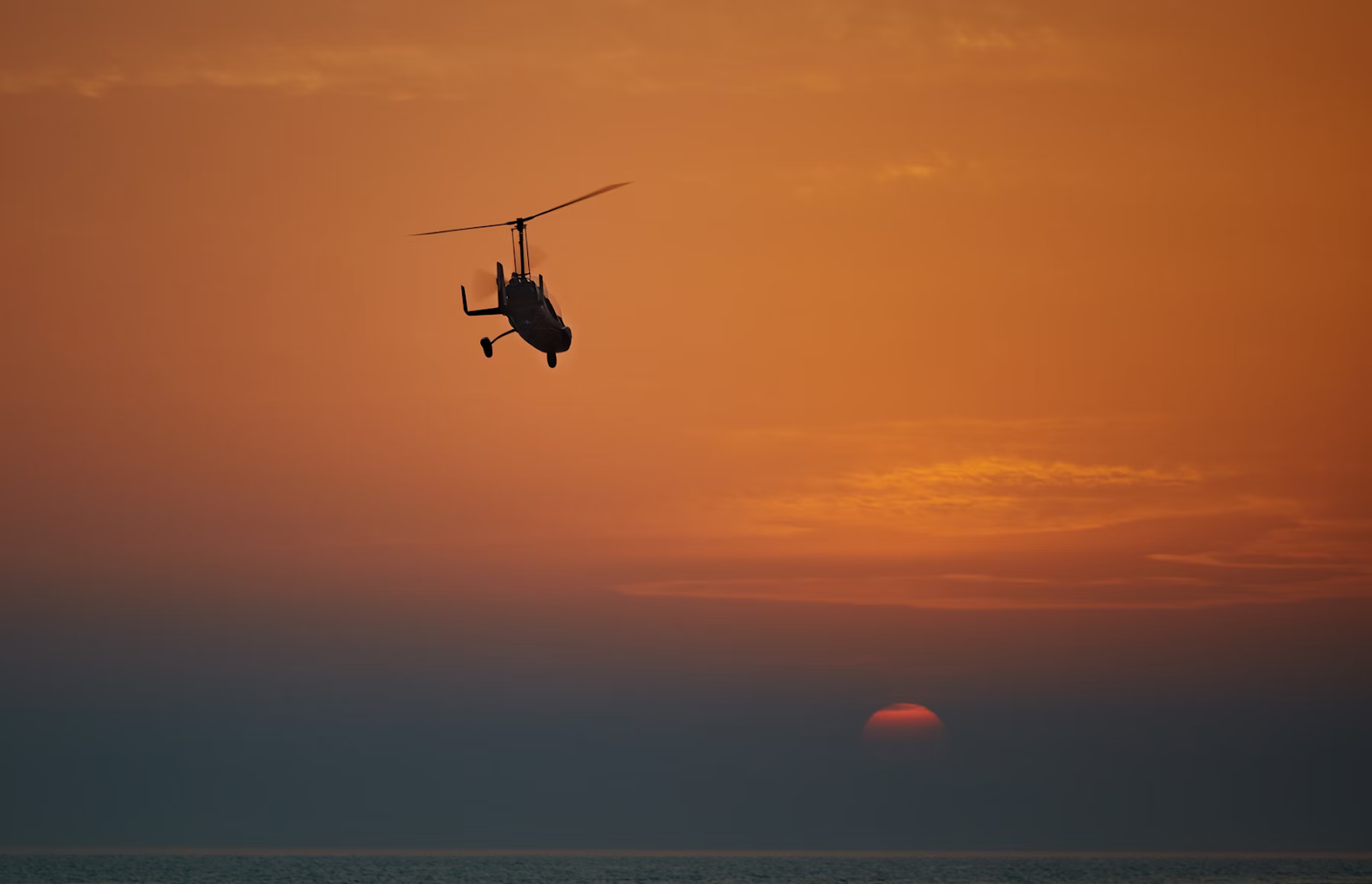 silhouette of a helicopter flying at sunset