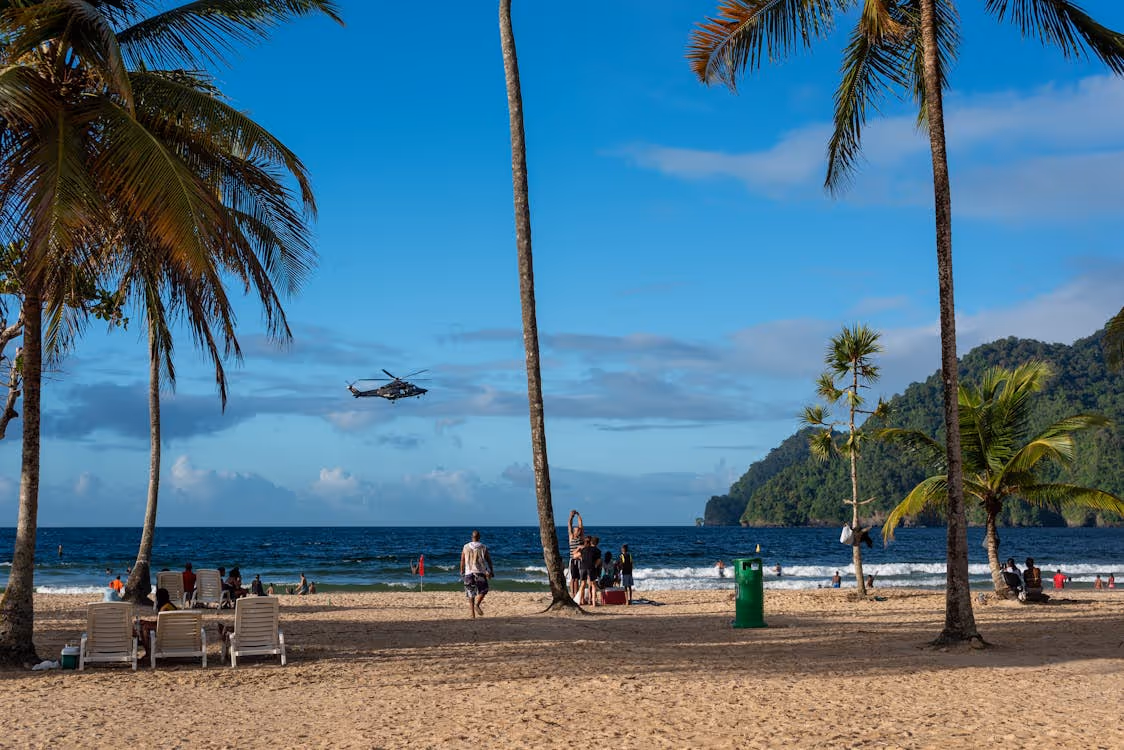 gray helicopter flying over a tropical beach in Trinidad and Tobago