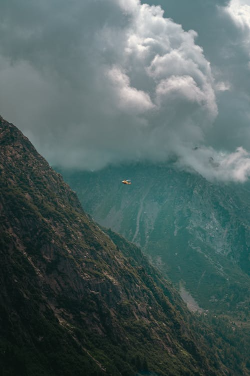 orange helicopter flying between two large smoke-covered mountains